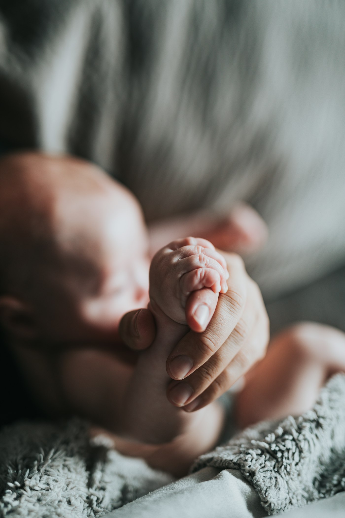 A newborn holding an adult's finger